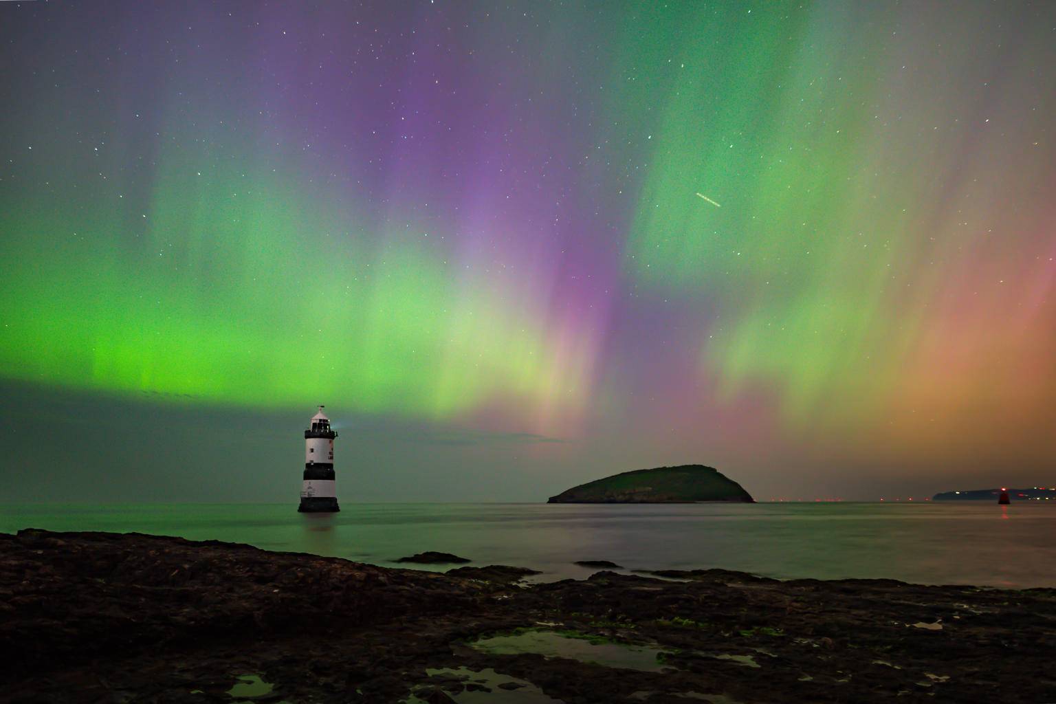  A photograph of Penmon lighthouse with the aurora lights in the back