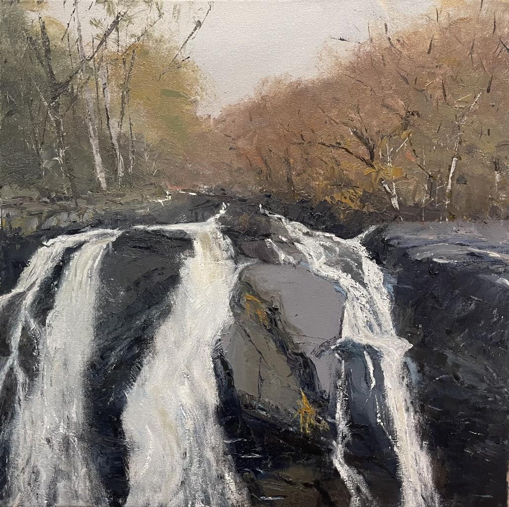 a waterfall over large rocks with brown and orange trees in the back