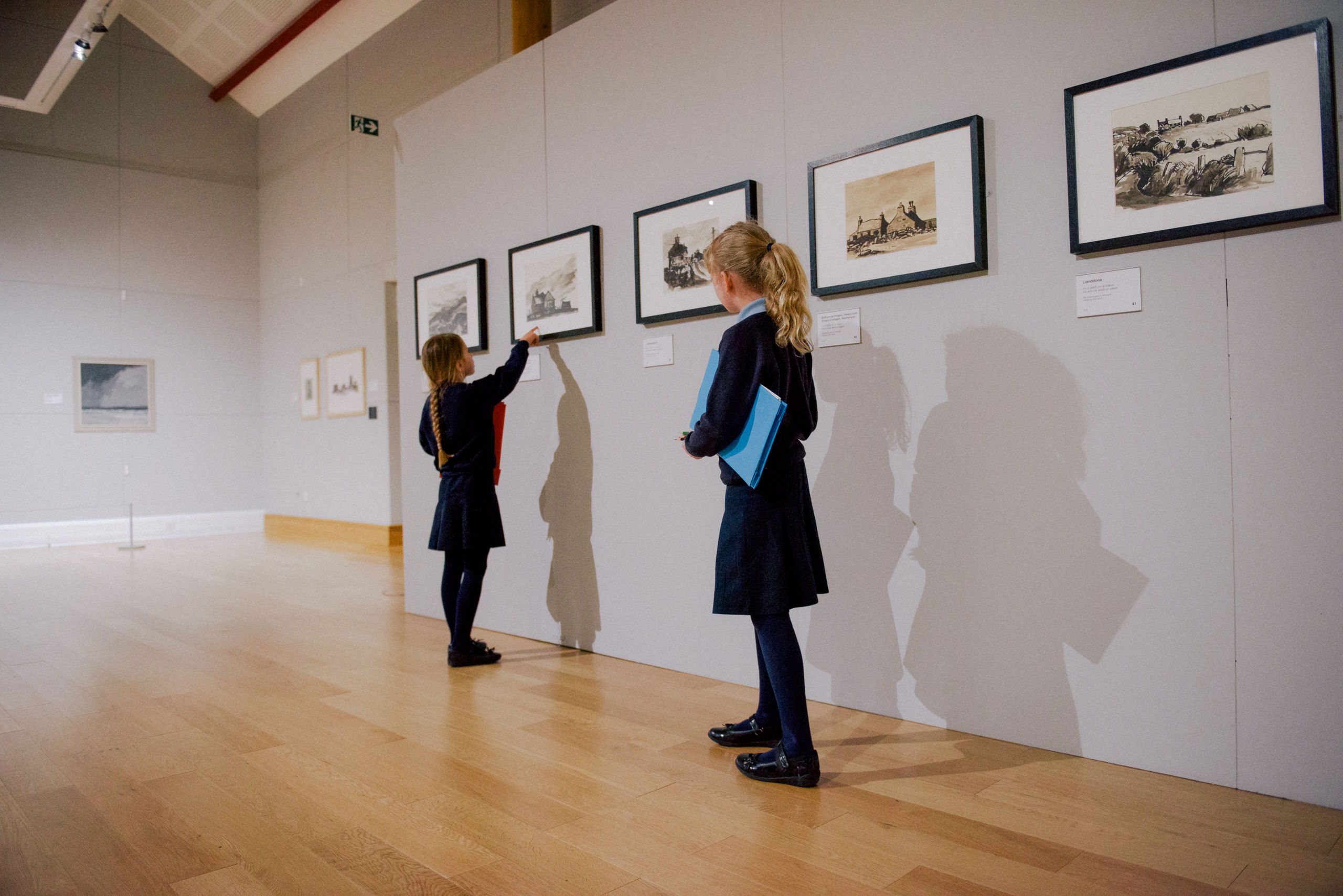 Two school pupils looking at art works in a gallery.