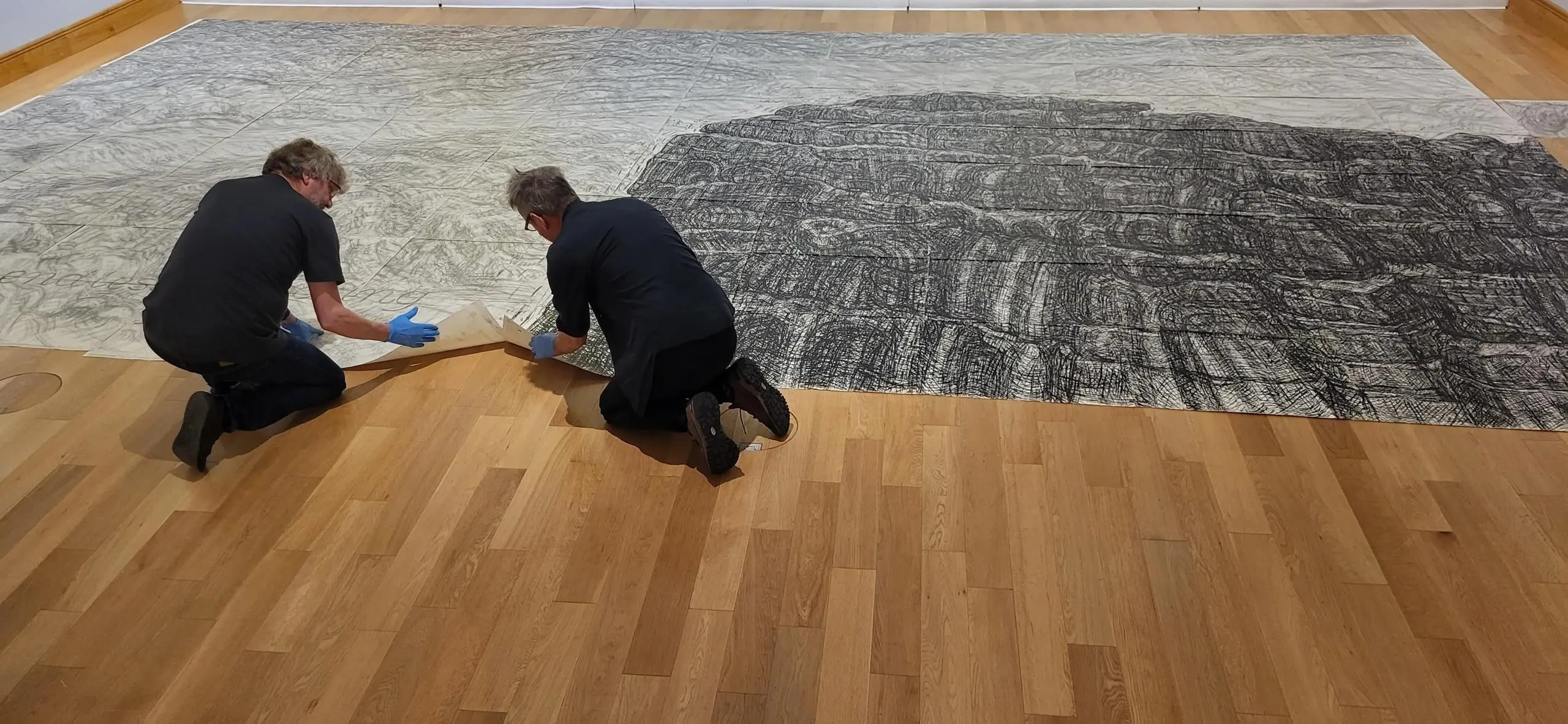 Staff arranging a huge drawing on the gallery floor